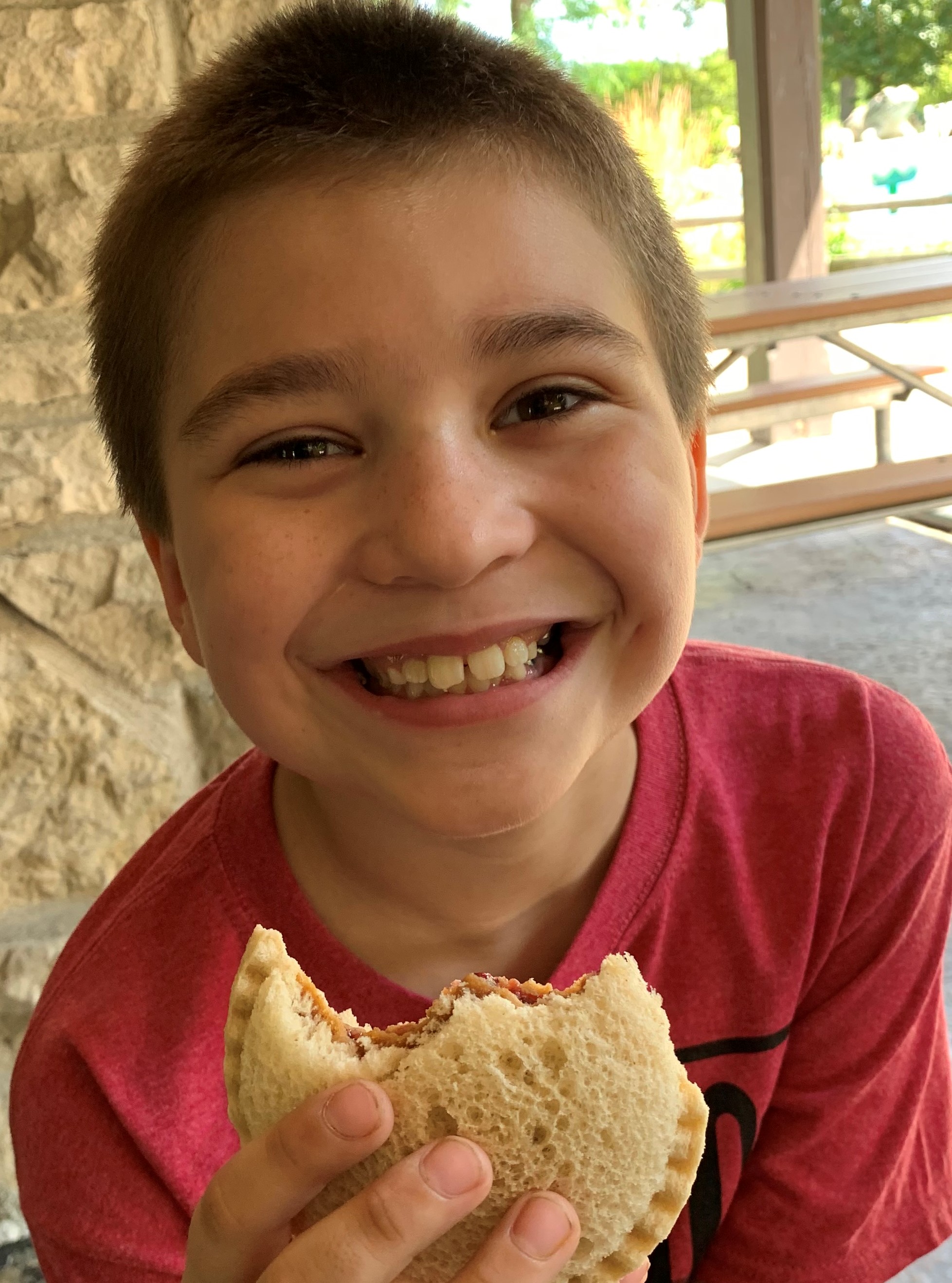 Smiling boy in red t-shirt eating PB & J sandwich