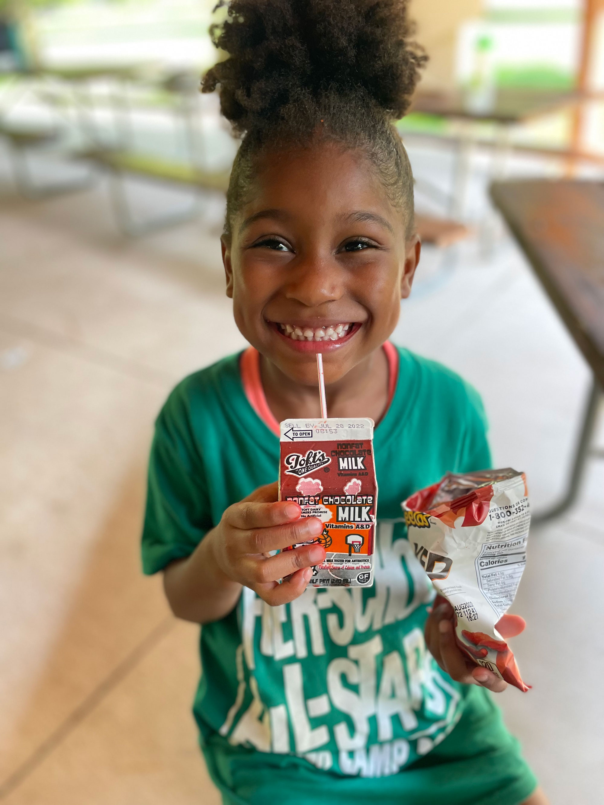 Smiling girl in green t-shirt drinking carton of milk