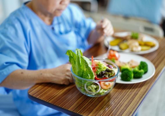 Elderly woman eating breakfast while sitting and hungry on bed in hospital