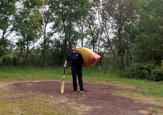 Megan Helsel carrying a kayak to the water, using a paddle as support