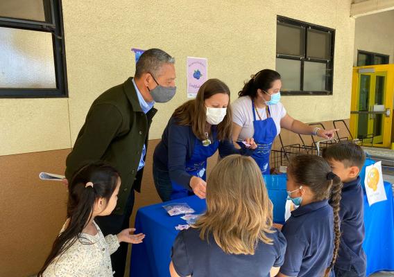 A man standing next to two women behind a table talking to four elementary school students