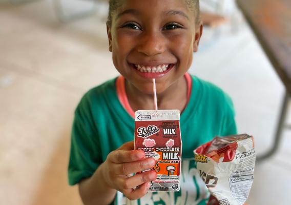 Smiling girl in green t-shirt drinking carton of milk