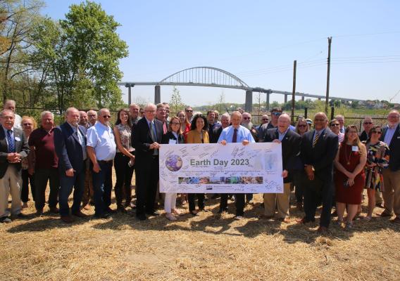 A group of people standing outside smiling with Earth Day 2023 sign