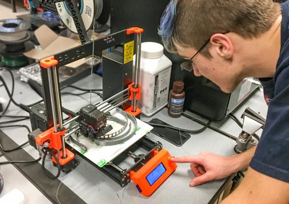 A 3D printer is adjusted by a technician at Somerset Community College